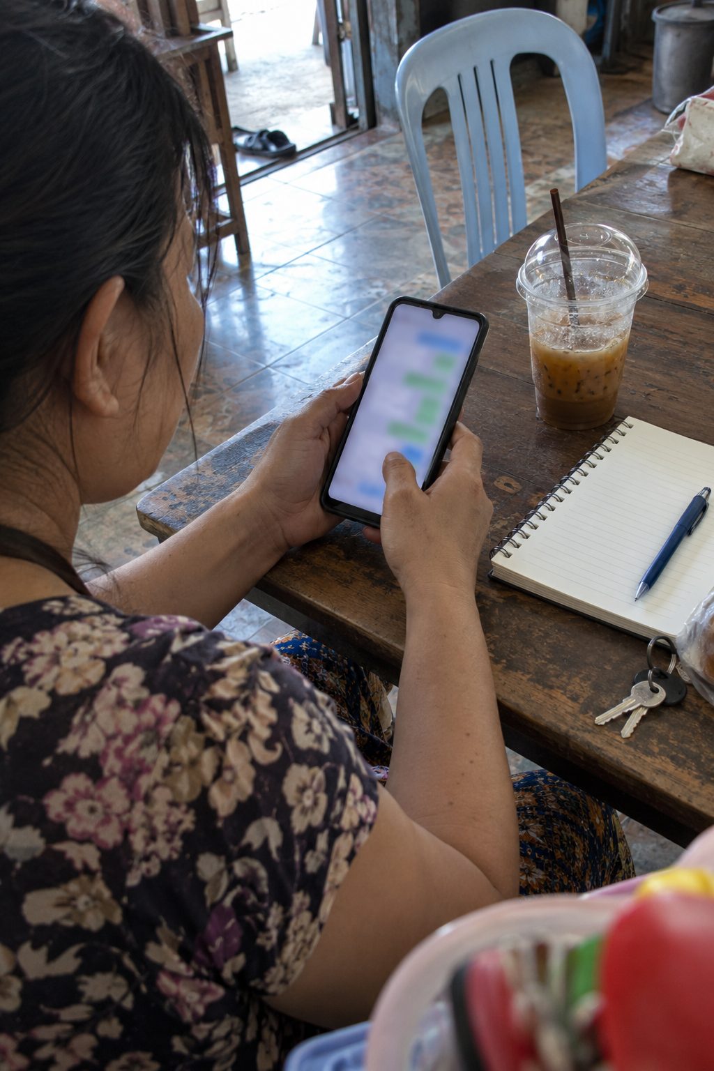 Hands hold a phone with a chat open, beside a glass of iced tea and a notebook on a wooden table.